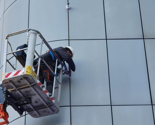 Camera installateur werkt kabels weg langs een gebouw op een hoogwerker